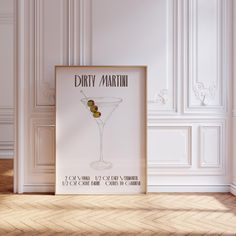 a framed poster with a martini glass on the floor in front of a white wall