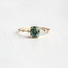 a gold ring with a green diamond in the center on a white surface, close up