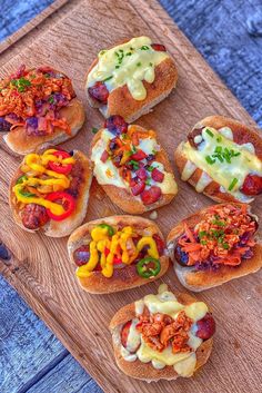 several hot dogs with toppings are on a wooden board