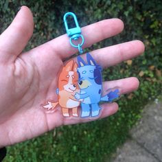 a hand holding a keychain with two cartoon cats on it's side