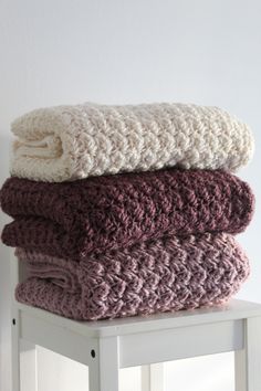 three crocheted blankets stacked on top of each other in front of a white wall