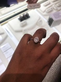 a person's hand with a diamond ring on top of their finger in front of a display case