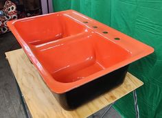 an orange and black square sink sitting on top of a wooden table next to a green wall