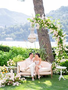 a man and woman sitting on a couch in front of a tree with white flowers