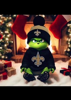 the grinch is sitting in front of a christmas tree with presents around him and wearing a new orleans saints sweater