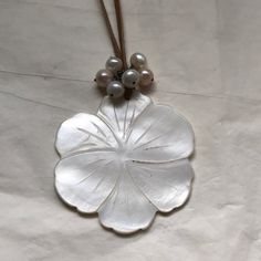 a white flower with pearls hanging from it's side on a brown string and some beads