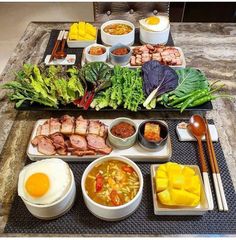 an assortment of food is displayed on a table with chopsticks, bowls and utensils