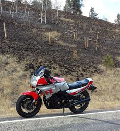 a red and silver motorcycle parked on the side of the road next to a hill