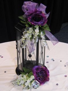 two purple flowers are sitting in a black lantern on a table with sequins