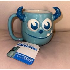 a blue mug with eyes and horns on it sitting next to a card that says abonsters