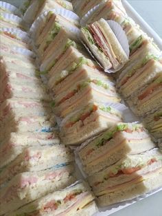 a platter filled with lots of sandwiches on top of white paper plates next to each other