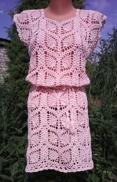 a pink crocheted dress is hanging on a clothes line in front of some bushes