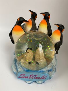 four penguins are standing in front of a snow globe with an inscription sea world on it