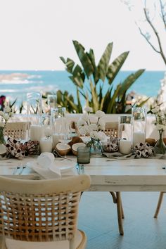 the table is set with candles, plates and glasses for dinner on the beach side