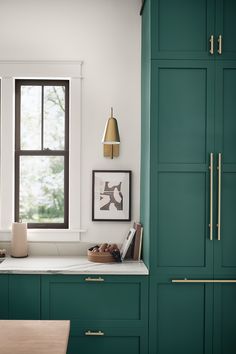 a kitchen with green cabinets and white counter tops in front of a window that has black framed pictures on it