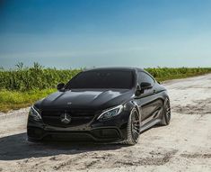 a black car parked on the side of a dirt road next to a corn field