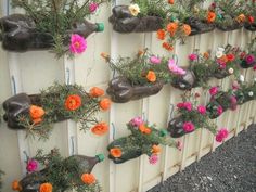 flowers are growing on the side of a wall that is decorated with plastic bottles and wire