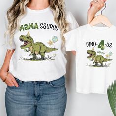 a woman wearing a white shirt and jeans holding up a t - shirt with an image of a dinosaur on it