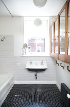 a bathroom with black and white tile flooring next to a bathtub, sink and window