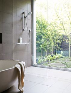 a bath tub sitting next to a glass door in a bathroom with trees outside the window