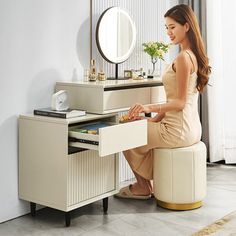 a woman sitting on a stool in front of a dressing table with drawers and a mirror