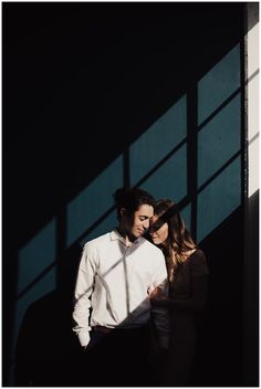 a man and woman standing next to each other in front of a wall with shadows on it