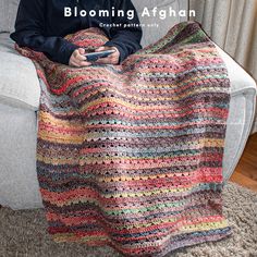 a man sitting on a couch holding a cell phone in his hand and a crocheted blanket draped over him