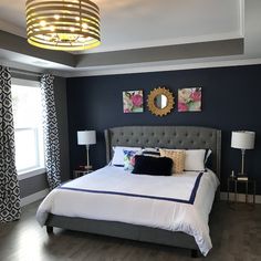 a bedroom with blue walls, white bedding and gray headboard is pictured in this image