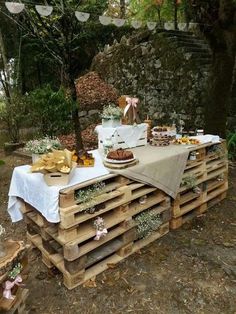 an outdoor table set up with food and decorations on top of wooden pallets in the woods