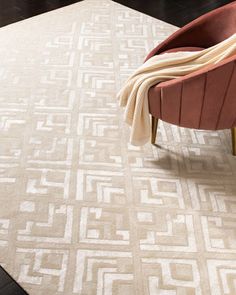 a white rug with an intricate design on the top and bottom, in front of a red chair