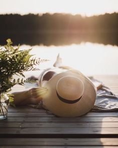 a person laying on top of a wooden deck next to a lake wearing a hat