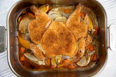 a chicken dish in a pan with carrots, onions and other vegetables on the side