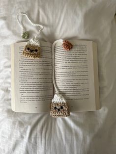 an open book with two crocheted animals hanging from it's sides on a bed