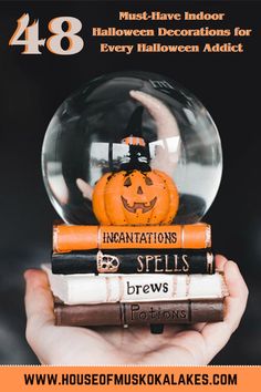 a hand holding a snow globe filled with books and a jack - o'- lantern