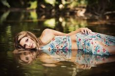 a beautiful young woman laying on top of a body of water wearing a blue dress