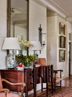 a living room filled with furniture next to a wall mounted mirror and vase on top of a wooden table