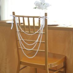 a chair with pearls on it and a flower vase in the back ground, sitting next to a window