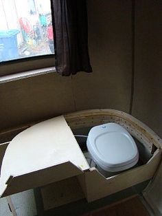 a white toilet sitting inside of a cardboard box on top of a wooden floor next to a window