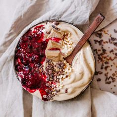 a bowl filled with yogurt and berries on top of a white cloth next to a wooden spoon