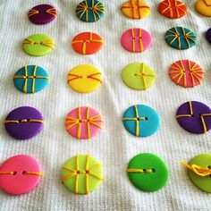 many different colored decorated cookies on a white tablecloth with yellow ribbons and bows around them