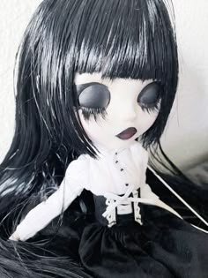 a doll with long black hair and big eyes sitting on a white surface next to a wall