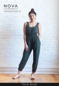 a woman standing in front of a white brick wall wearing green jumpsuits and sandals