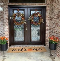 two potted plants are sitting on the front porch with welcome mats and wreaths