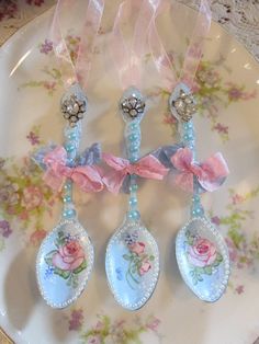 three spoons on a plate decorated with pink flowers and bows are hanging from ribbons