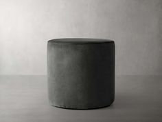 a grey stool sitting on top of a floor next to a white wall and window