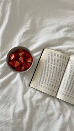 a bowl of strawberries next to an open book