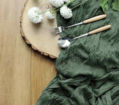 flowers and utensils are laid out on a wooden table with green fabric draped over it