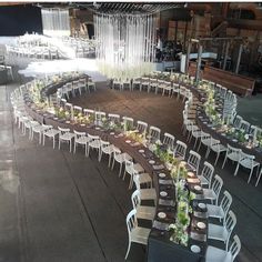 a circular table set up with white chairs and green centerpieces for an event