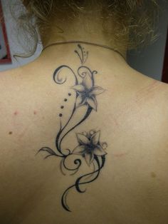 the back of a woman's neck with flowers and swirls tattoo on it