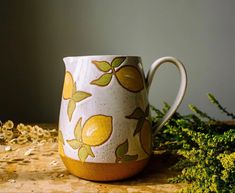 a yellow and white mug sitting on top of a wooden table next to green plants